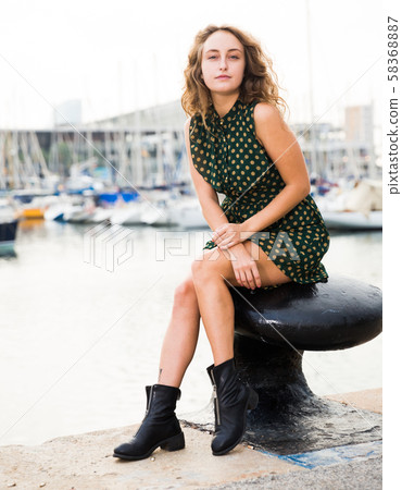 Young girl tourist in dress sitting at stone bench in port with boats 58368887