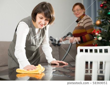 Woman wiping table, elderly mother vacuum cleaning sofa Woman wiping table, elderly mother vacuum cleaning sofa 58369051