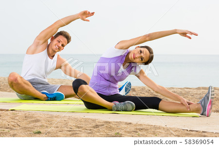 Smiling woman and guy training on beach by sea Smiling woman and guy training on beach by sea 58369054