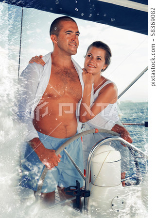 Couple standing at yacht wheel along coast of Barcelona Couple standing at yacht wheel along coast of Barcelona 58369082