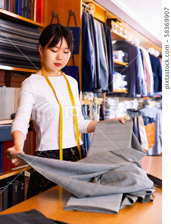 Chinese young female seller of fabric shop showing new trendy textiles of high quality for dressmaking Chinese young female seller of fabric shop showing new trendy textiles of high quality for dressmaking 58369907