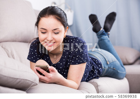 Happy woman on sofa with smartphone Happy woman on sofa with smartphone 58369938
