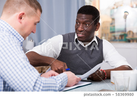 Two businessmen in home interior filling up documents Two businessmen in home interior filling up documents 58369980