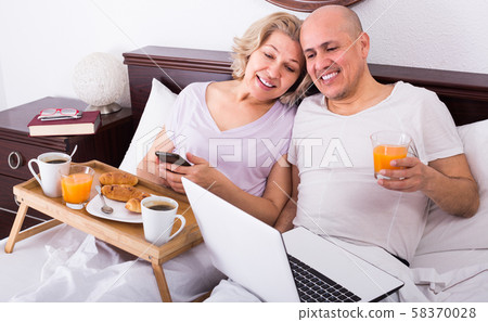Couple with laptop during breakfast in bed. Couple with laptop during breakfast in bed. 58370028