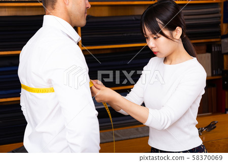Chinese woman tailor using measurement tape with client in mens cloths store Chinese woman tailor using measurement tape with client in mens cloths store 58370069