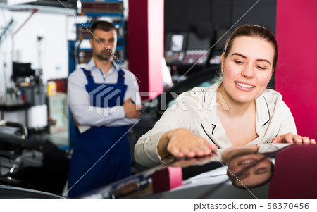 Happy woman touching surface of repainted car 58370456