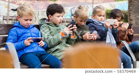 Kids playing with smartphones on bench Kids playing with smartphones on bench 58370469