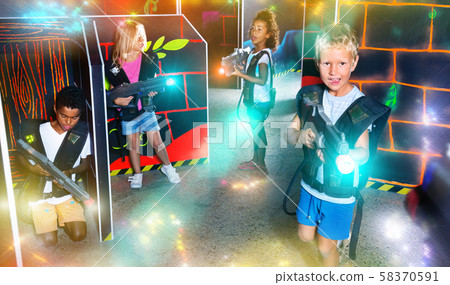 Preteen girls and boys with laser pistols playing laser tag Preteen girls and boys with laser pistols playing laser tag 58370591