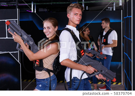 Team of laser tag guy and girl with laser pistols and friends in background Team of laser tag guy and girl with laser pistols and friends in background 58370704