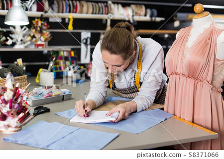 Woman professional sewer writing information about measuring textile Woman professional sewer writing information about measuring textile 58371066