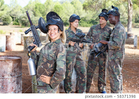Young woman wearing uniform and holding gun ready for playing paintball with friends outdoor Young woman wearing uniform and holding gun ready for playing paintball with friends outdoor 58371398