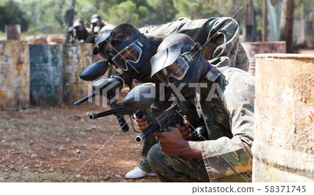 Paintball players aiming with gun in shootout outdoors Paintball players aiming with gun in shootout outdoors 58371745