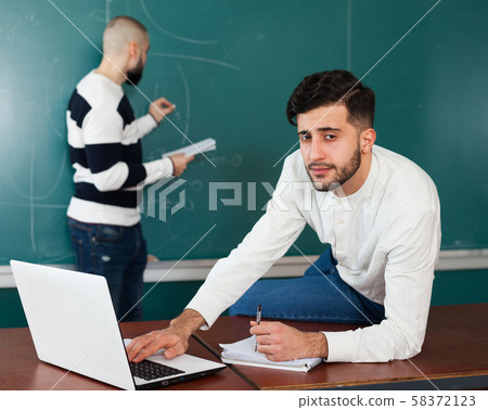 Students working with laptop near blackboard 58372123