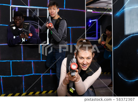 Emotional girl with laser pistol playing laser tag with multinational team Emotional girl with laser pistol playing laser tag with multinational team 58372307
