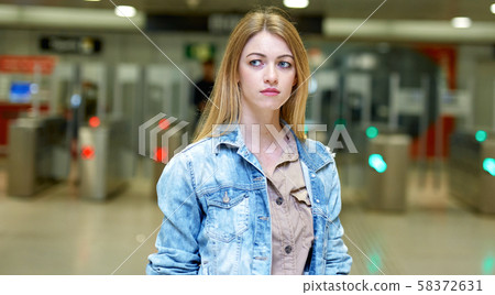 Blonde with long hair stands near the turnstiles at subway station 58372631