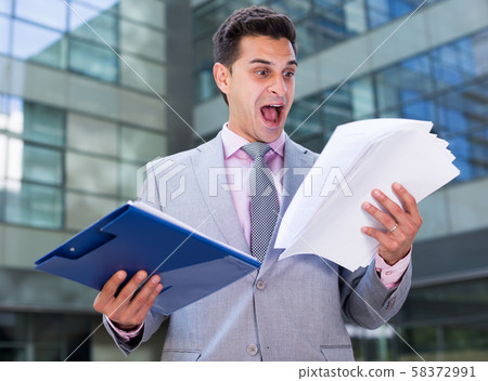 Dissatisfied businessman holding papers 58372991