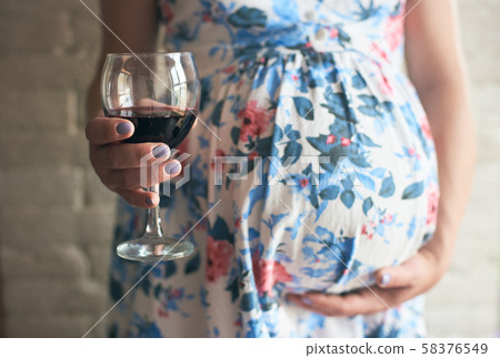 Selective focus of glass of wine in hands of pregnant woman 58376549