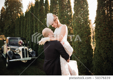 Happy newlywed couple, man and wife kissing near stylish retro car Happy newlywed couple, man and wife kissing near stylish retro car 58376839