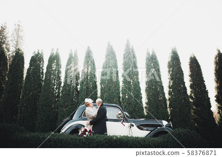 Happy newlywed couple, man and wife kissing near stylish retro car Happy newlywed couple, man and wife kissing near stylish retro car 58376871