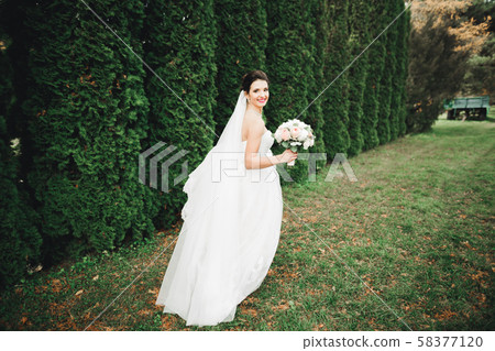 Beautiful bride in elegant white dress holding bouquet posing in park Beautiful bride in elegant white dress holding bouquet posing in park 58377120