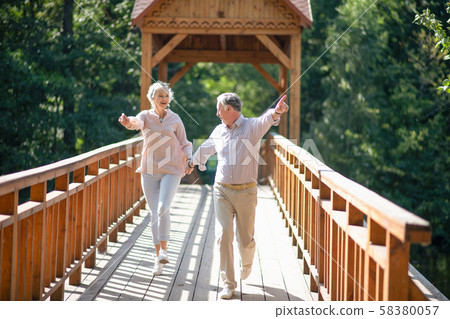 Mature adults running while crossing the bridge and feeling excited 58380057