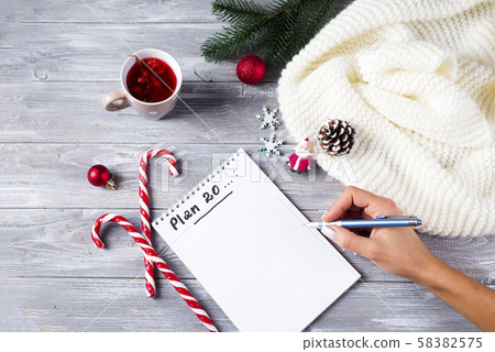 Hand of woman writing on notepad Christmas greetings with tea, decoration on wooden background 58382575