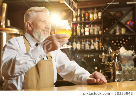 Barman holding beer glass, standing at bar counter. Barman holding beer glass, standing at bar counter. 58383948