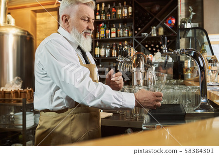 Barman standing at bar counter pouring beer in glass. Barman standing at bar counter pouring beer in glass. 58384301