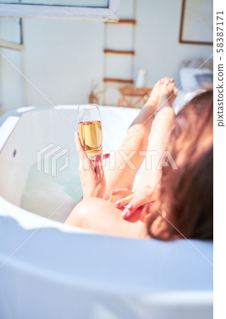 Photo from back of woman with wine glass with champagne in her hands lying in bath. Photo from back of woman with wine glass with champagne in her hands lying in bath. 58387171
