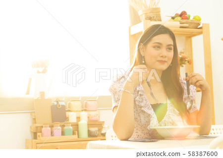young and happy Asian woman eating healthy soup sitting on the table in the kitchen with warm light from morning sunshine with copy space 58387600