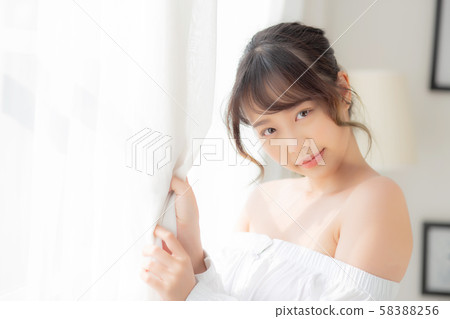 Portrait of beautiful young asian woman standing the window and smile while wake up Portrait of beautiful young asian woman standing the window and smile while wake up 58388256