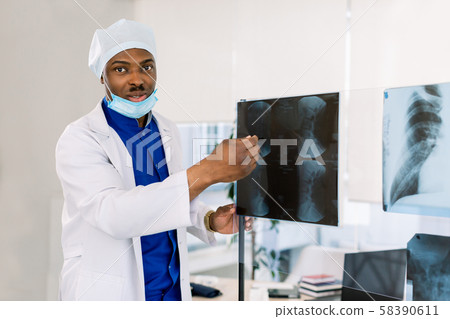 Portrait of young African male doctor surgeon or radiologist looking at a radiography Portrait of young African male doctor surgeon or radiologist looking at a radiography 58390611