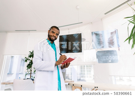 health and medicine concept - smiling African man doctor studying x-ray of the patients while health and medicine concept - smiling African man doctor studying x-ray of the patients while 58390661