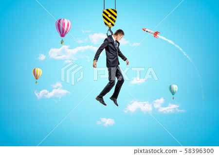 Businessman hanging on construction crane hook with hot air balloons and silver red space rocket in Businessman hanging on construction crane hook with hot air balloons and silver red space rocket in 58396300