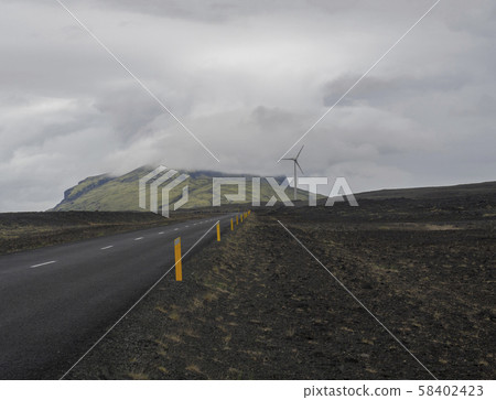 Asphalt road through empty northern volcanic landscape in iceland with Wind turbine and green hills Asphalt road through empty northern volcanic landscape in iceland with Wind turbine and green hills 58402423