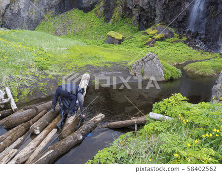 man hiker standing on wooden log takeing up clean water, filling 58402562