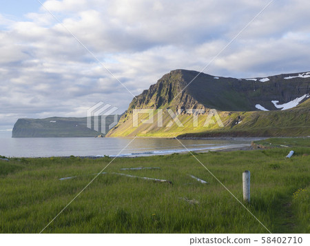Hloduvik cove sea shore with green grass meadow, Skalarkambur mountain, wooden logs and footpath 58402710