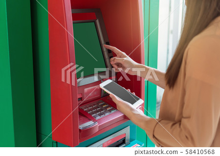 woman using the smart mobile phone for withdrawing in front of the ATM, business Automatic Teller Machine concept woman using the smart mobile phone for withdrawing in front of the ATM, business Automatic Teller Machine concept 58410568