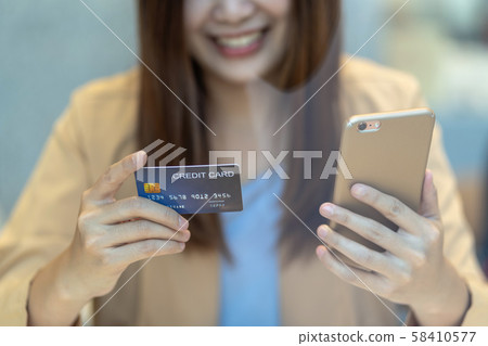 Closeup Asian woman using credit card with mobile for online shopping in department store over the clothes shop store background, technology money wallet and online payment concept, credit card mockup Closeup Asian woman using credit card with mobile for online shopping in department store over the clothes shop store background, technology money wallet and online payment concept, credit card mockup 58410577