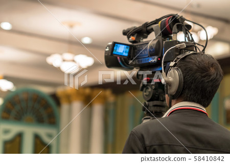 Rear side of Video Cameraman taking photograph to Asian Speaker with casual suit on the stage present the screen in the conference hall or seminar meeting, event and seminar production concept Rear side of Video Cameraman taking photograph to Asian Speaker with casual suit on the stage present the screen in the conference hall or seminar meeting, event and seminar production concept 58410842