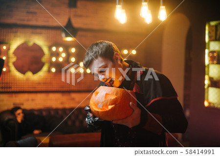 Young man in a Halloween costume of Count Dracula holds a carved festive pumpkin Young man in a Halloween costume of Count Dracula holds a carved festive pumpkin 58414991