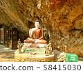 Buddha statue standing in a recess of a rock. Nearby is a donation box and two wooden bookcases. Buddha's face illuminated by the bright sun                               58415030