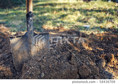 Old spade or shovel stuck in freshly dug earth 58416709