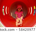 A little girl in clothes with hearts and an unusual facial expression rides on a red slide  58420977