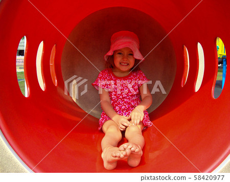 A little girl in clothes with hearts and an unusual facial expression rides on a red slide  58420977