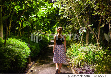 woman walking in a park with tropical trees at 58422210