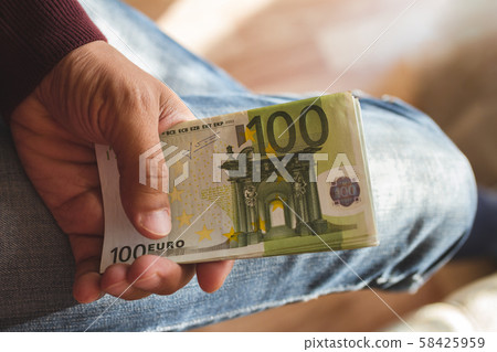 one hundred euro banknotes in tanned left hand of man in burgundy sweater against the background of one hundred euro banknotes in tanned left hand of man in burgundy sweater against the background of 58425959