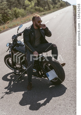 Sexy brutal biker posing on the bike backwards smoking sigar Sexy brutal biker posing on the bike backwards smoking sigar 58428268