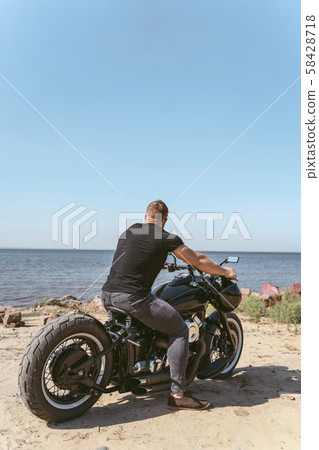 Back view of an athletic biker sitting on bike looking at the ocean Back view of an athletic biker sitting on bike looking at the ocean 58428718