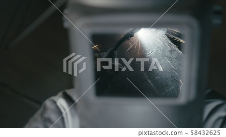 Forge workshop. Smithy. Worker in a welding hood helmet welds a part by electric welding. Sparks are 58432625